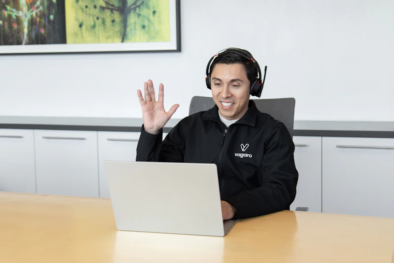 Freundlicher Ansprechpartner mit Headset winkt vor seinem Laptop