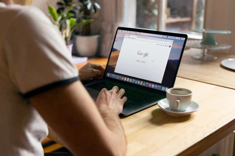 Person tippt eine Suchanfrage in einen Laptop, daneben eine Tasse Kaffee